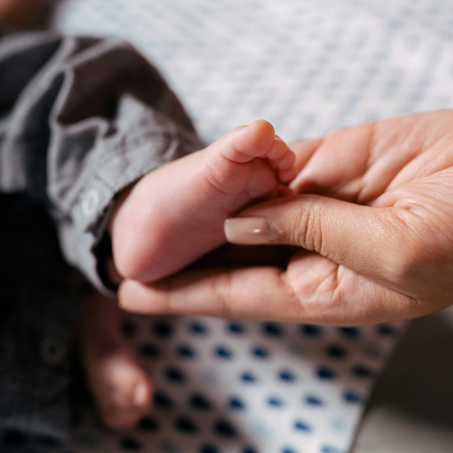 Toddler receiving Reflex when adjusting to life with a baby brother. blonde haired white toddler in Baby Moses basket receiving reflexology by adult caregiver.